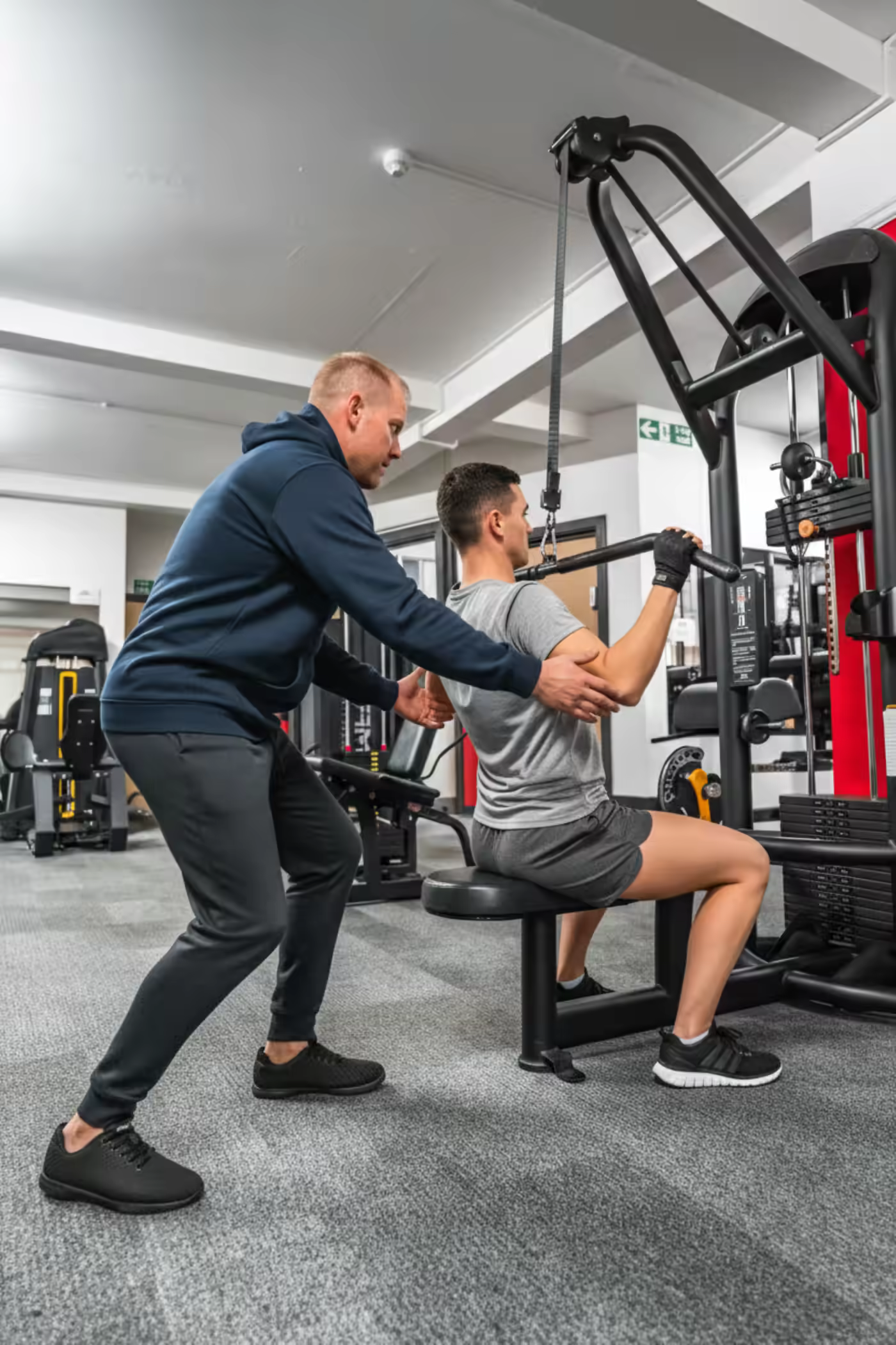 A trainer correcting a client's form on a cable machine