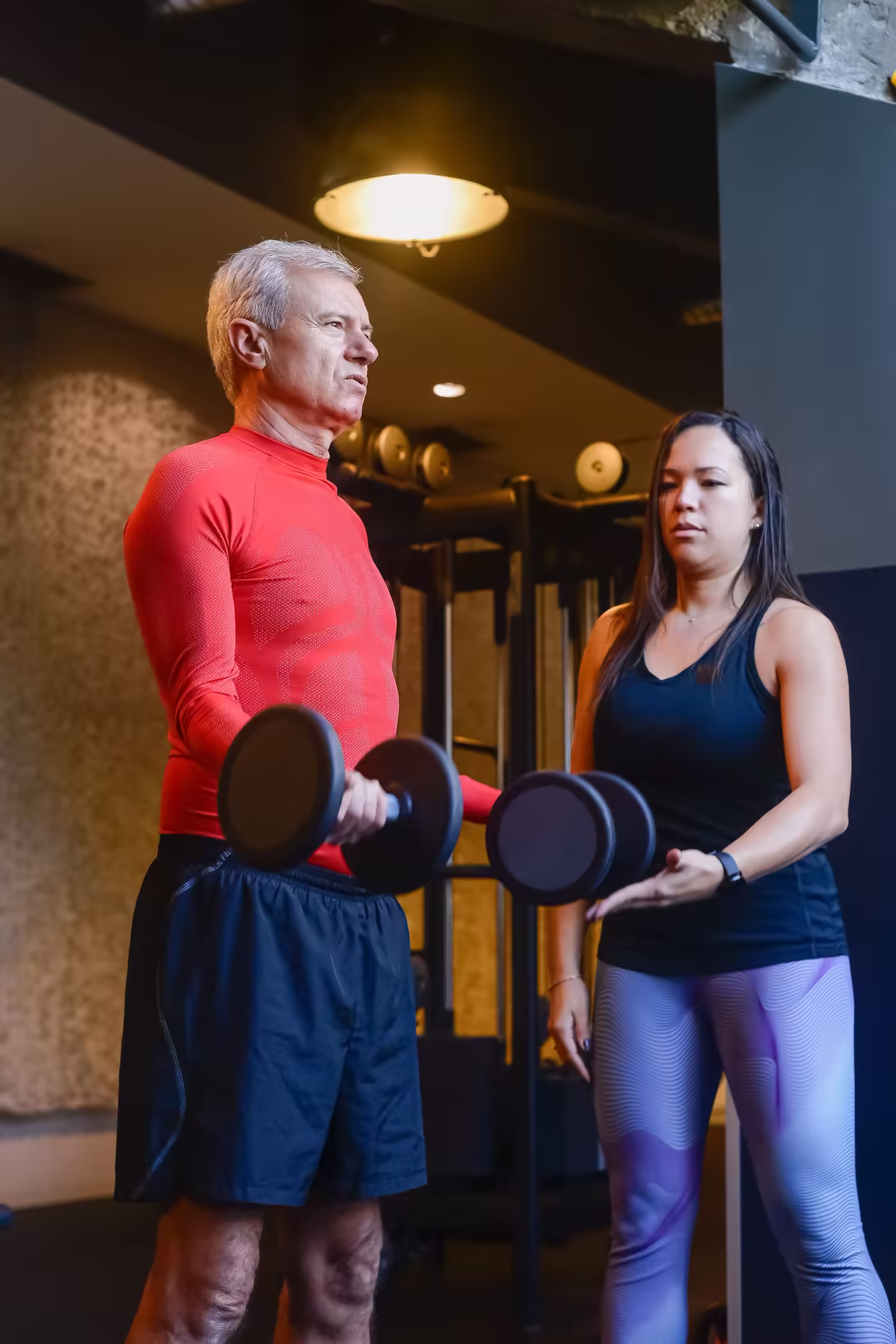 A trainer guiding an older client through dumbbell curls